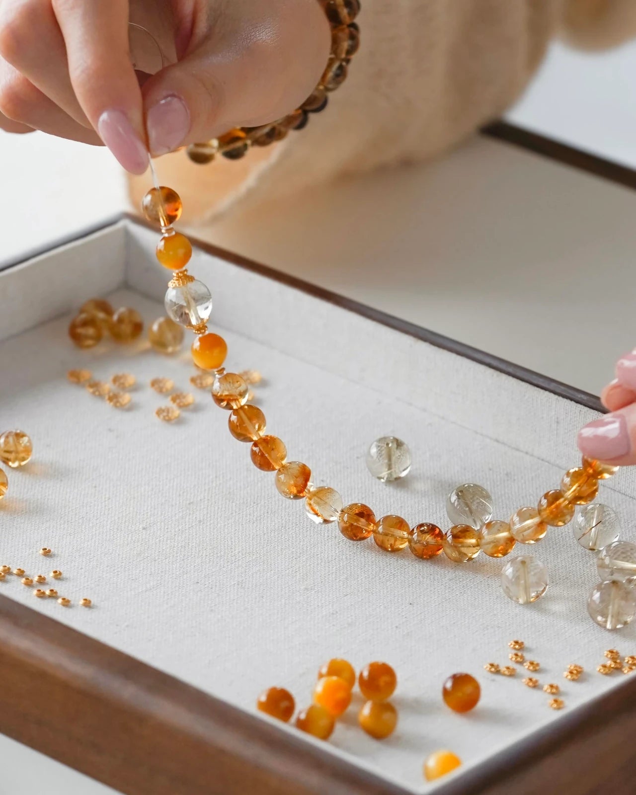 Handcrafted close-up—hands stringing a citrine, rutilated quartz and tiger eye beaded stretch bracelet on elastic cord.
