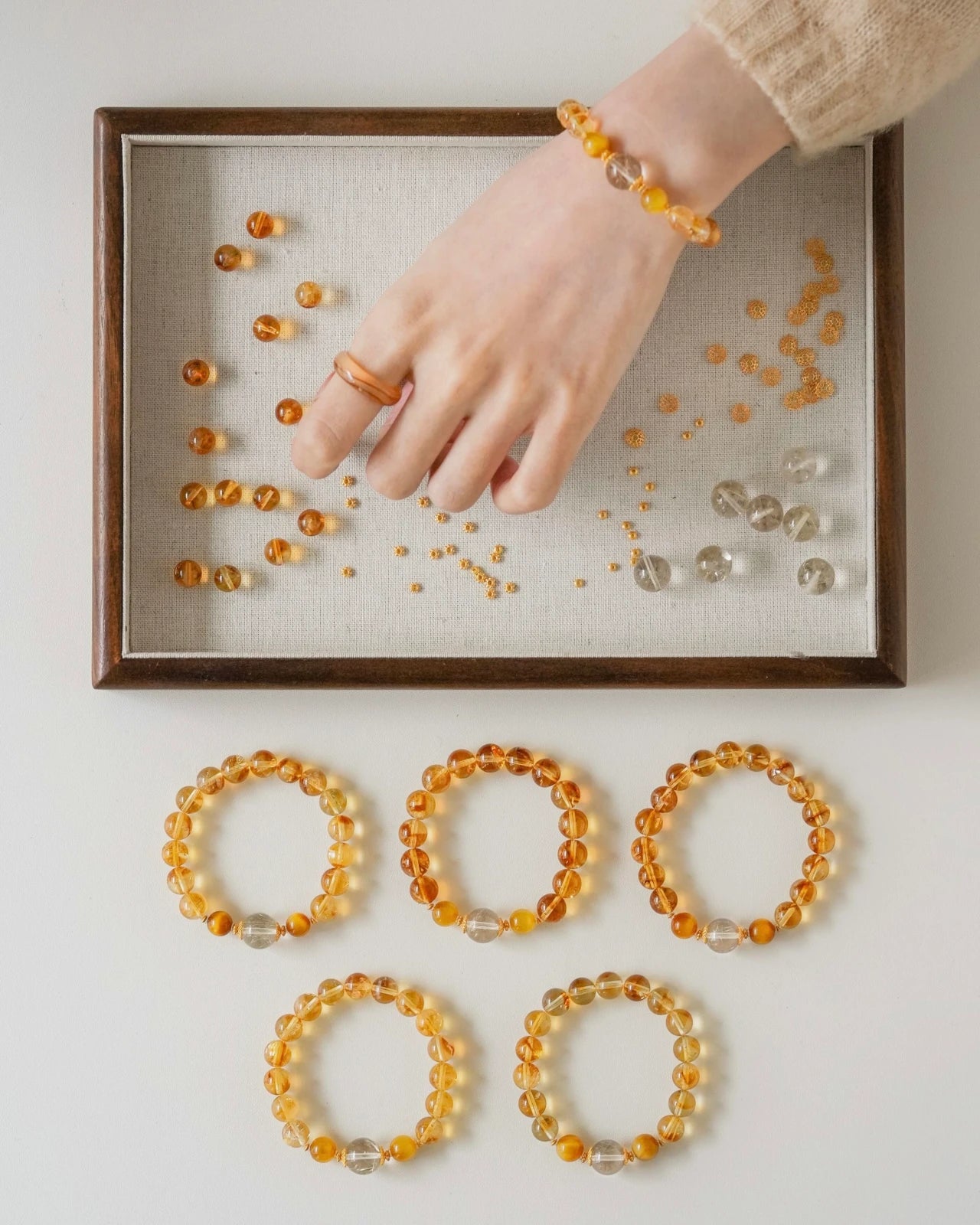 Studio wrist shot—citrine beaded stretch bracelet with rutilated quartz and tiger’s eye accents, gold-plated S925; hand above bead tray.