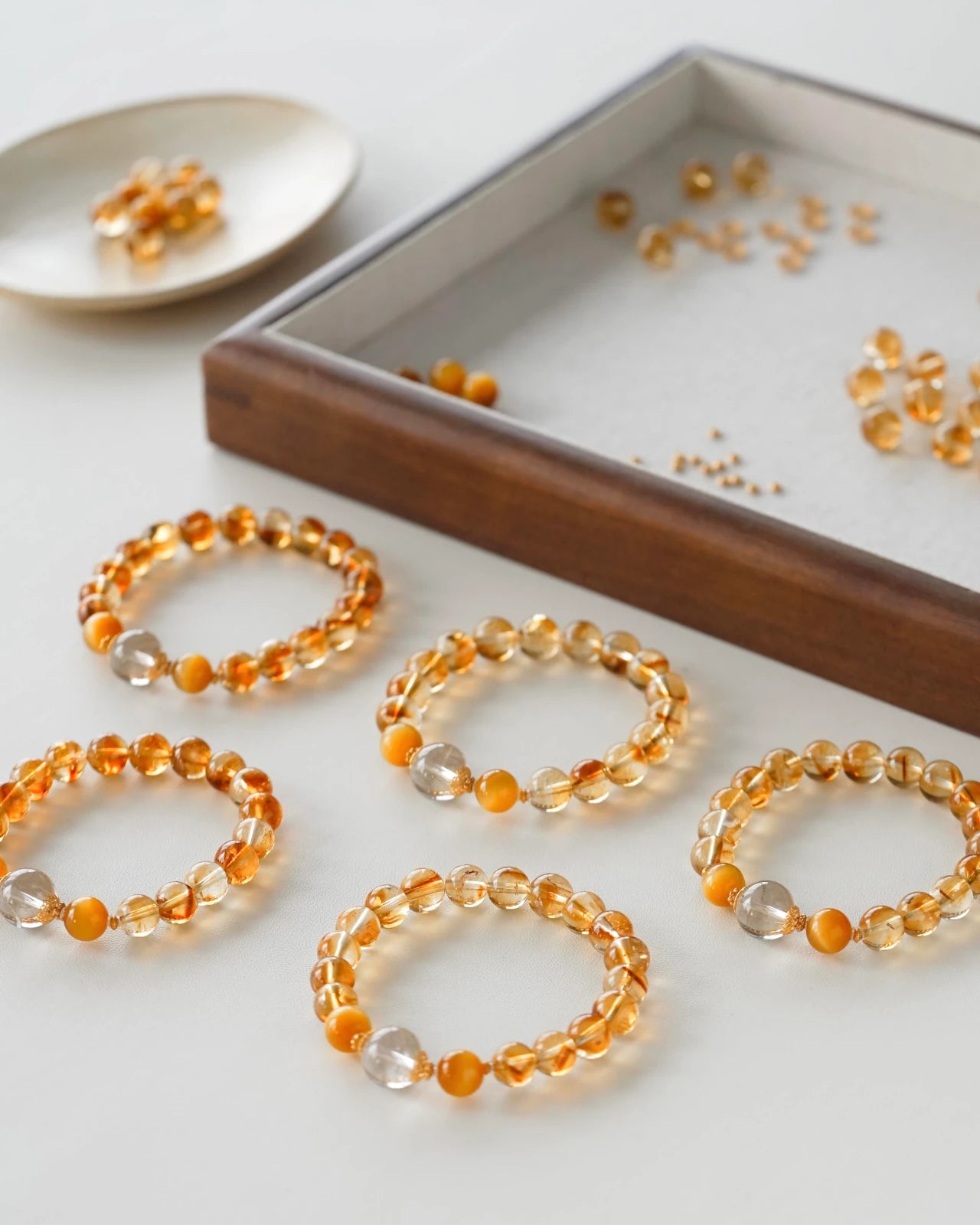 Flat lay set—multiple citrine beaded stretch bracelets with rutilated quartz and tiger eye accents arranged beside a wooden bead tray