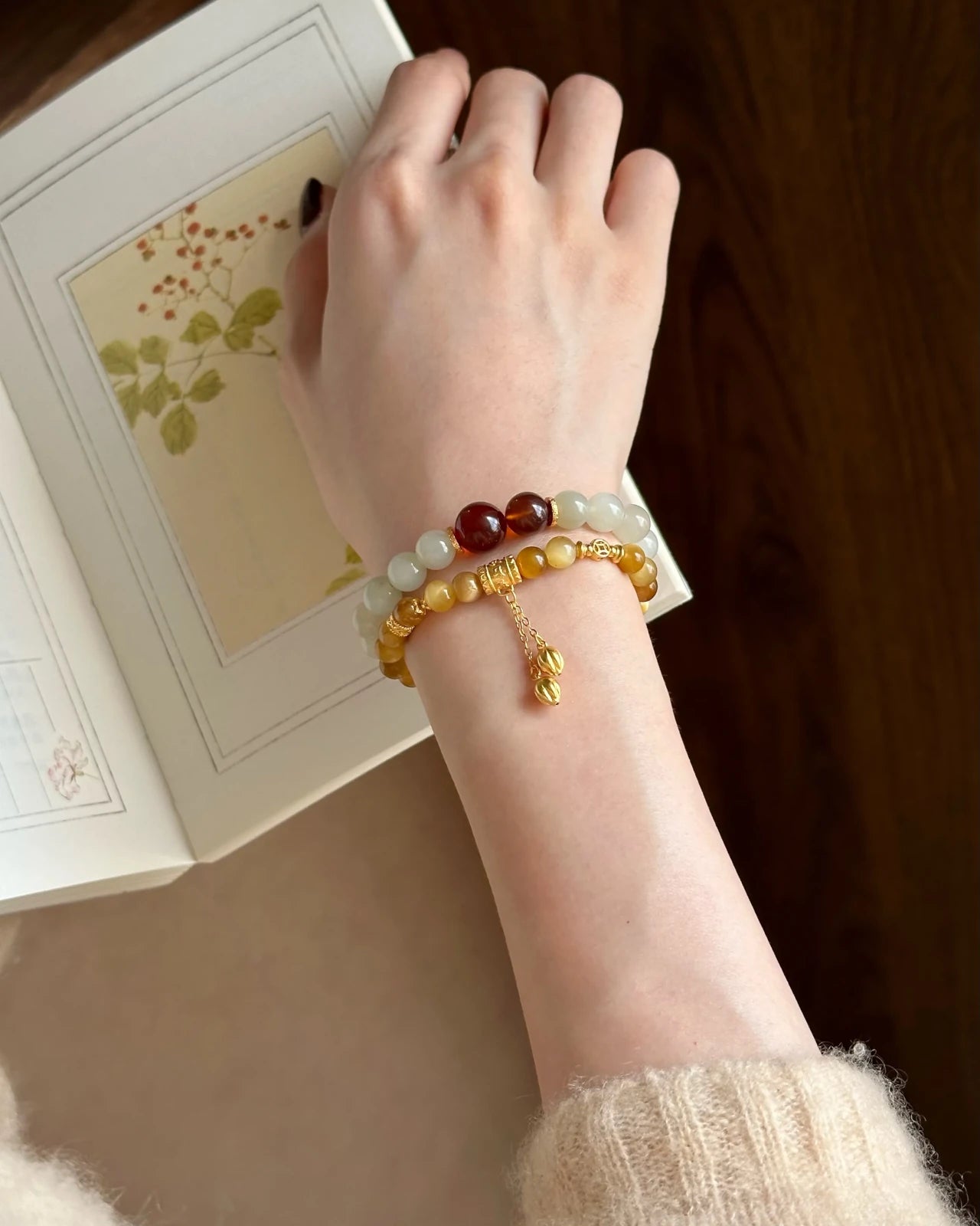 Wrist stack lifestyle—6mm golden tigers eye stretch bracelet with gold-plated S925 accents and charm chain, shown while reading; stacking bracelet for protection and focus.