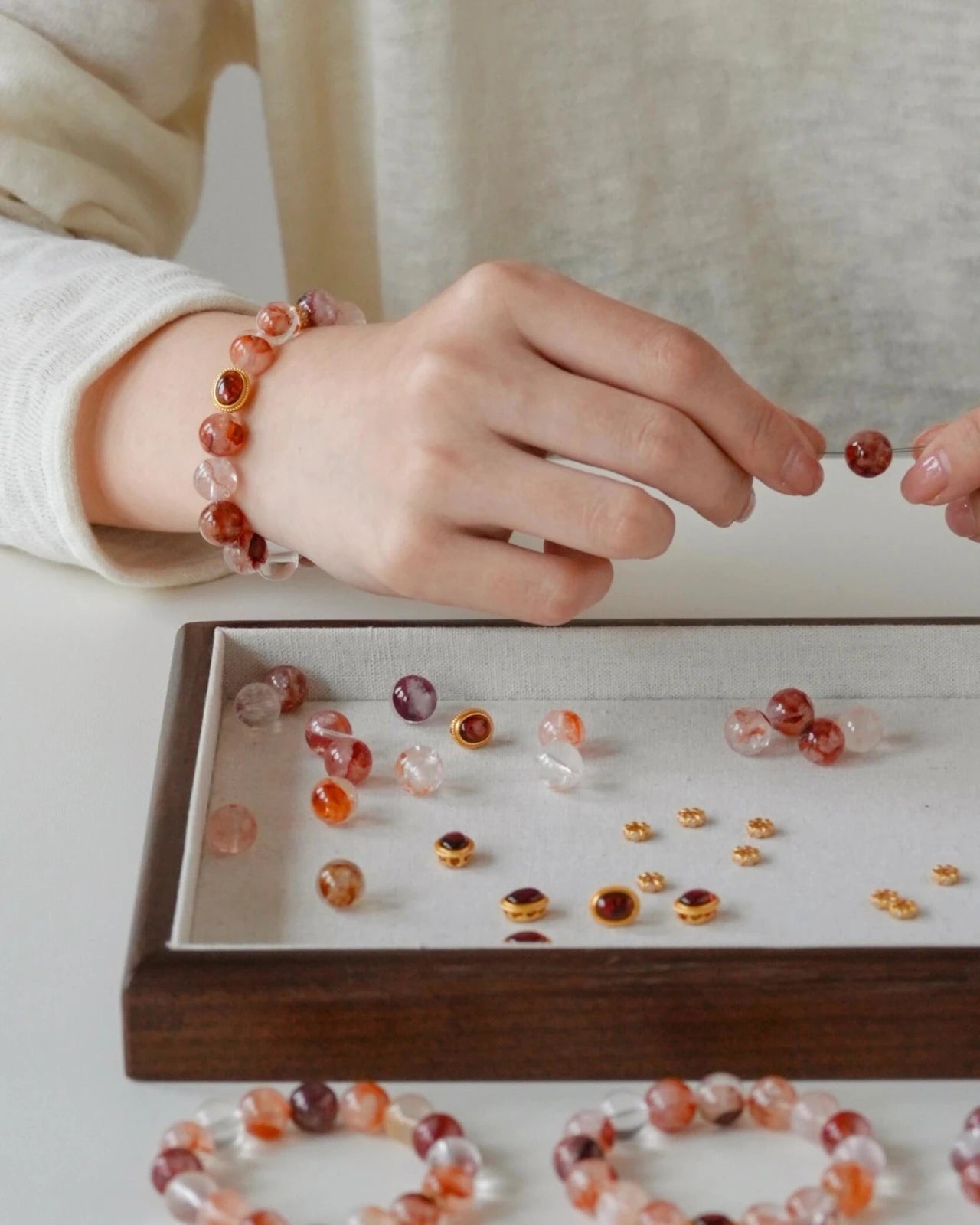 Close-up crafting—choosing hematoid quartz beads beside garnet charms and small gold findings