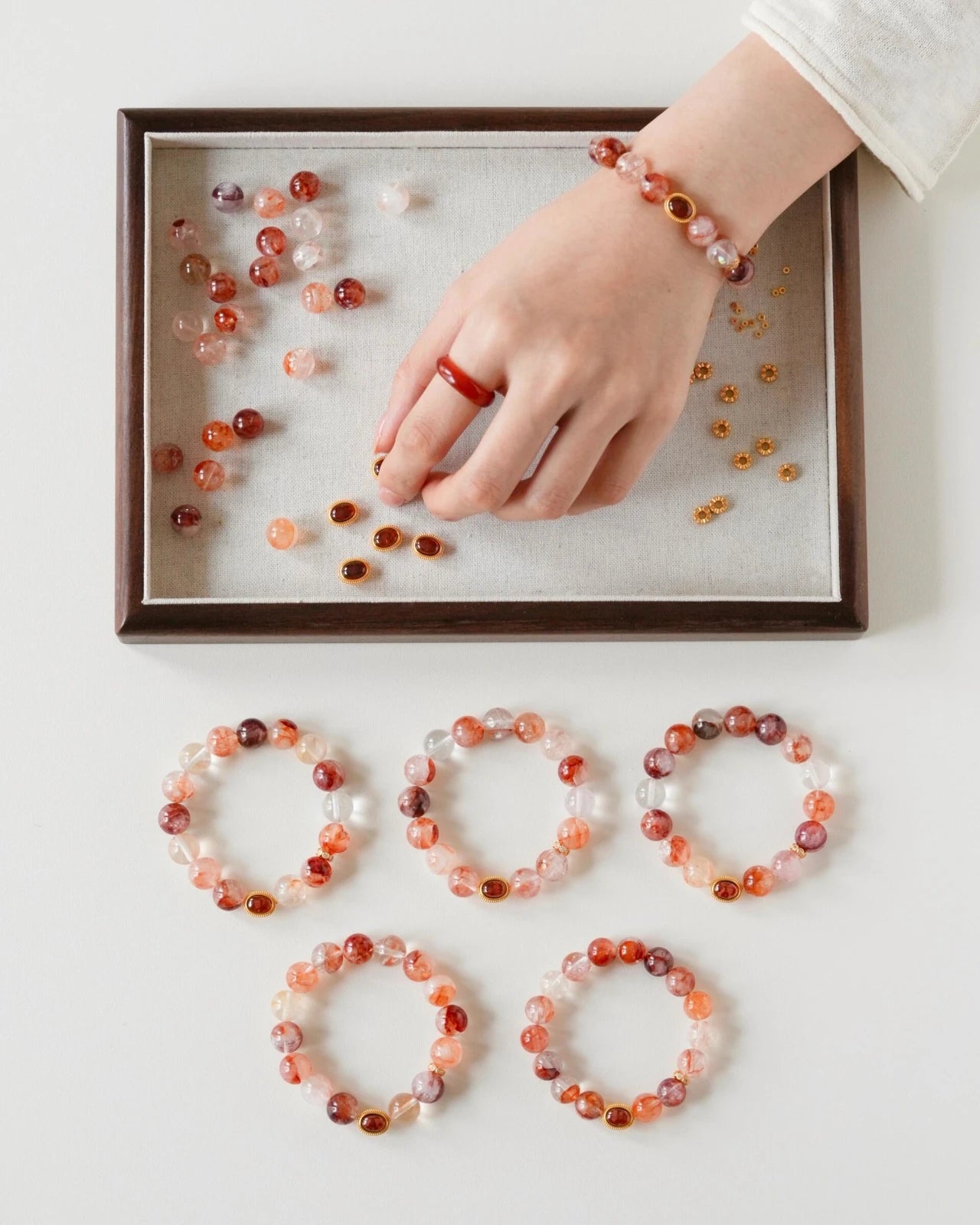 Hand assembling hematoid quartz bracelet—garnet cabochon charm and gold spacers in a tray