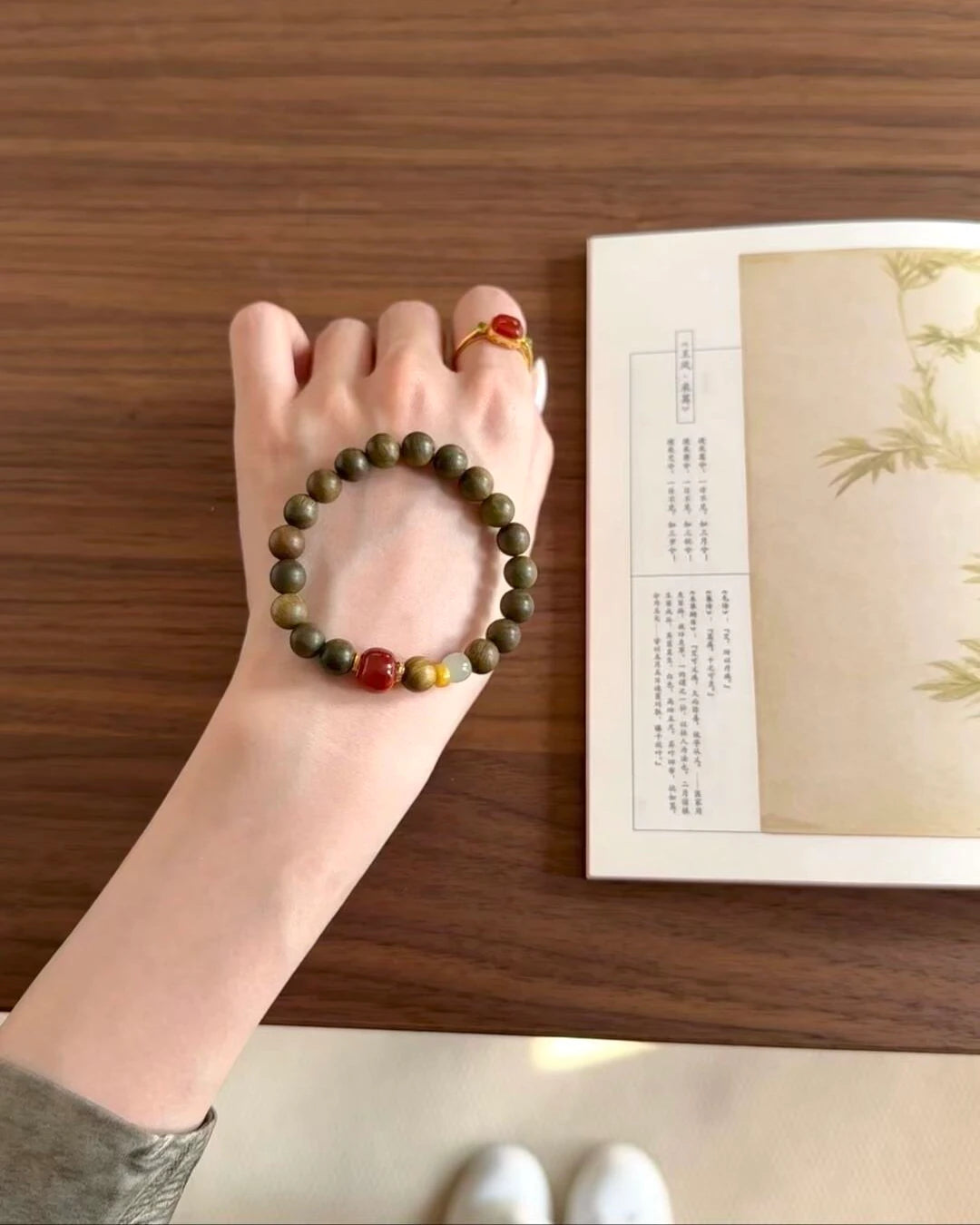 Hand holding the Vital Harmony Bracelet, highlighting red agate focal with amber and jade accents.