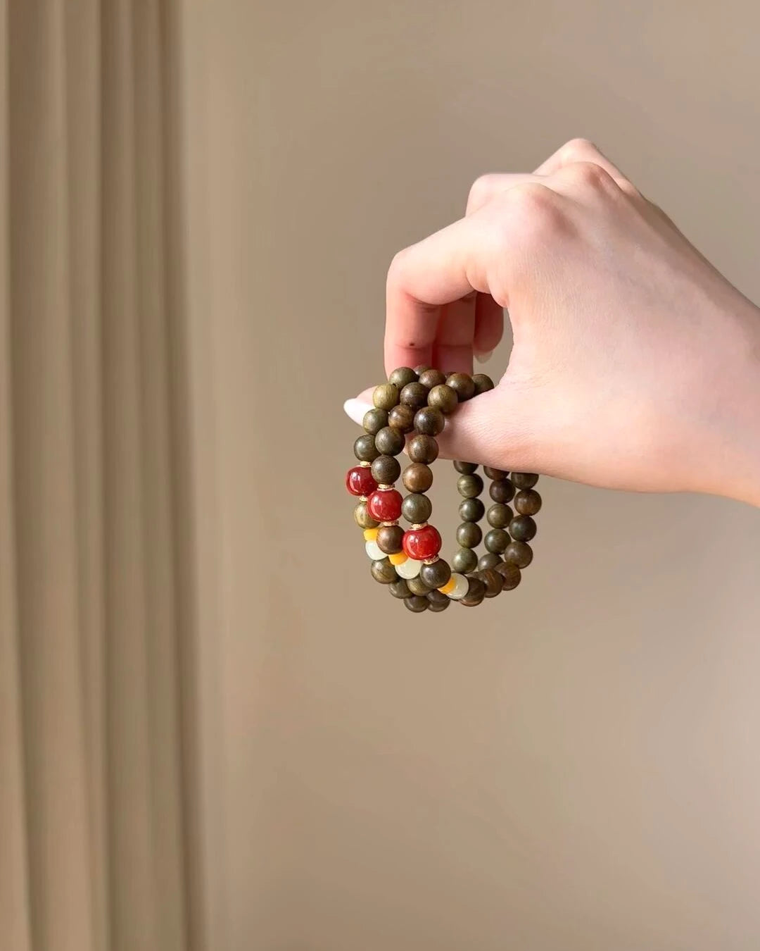 Hand holding multiple Vital Harmony Bracelets; sandalwood beads with red agate, amber, and jade accents.