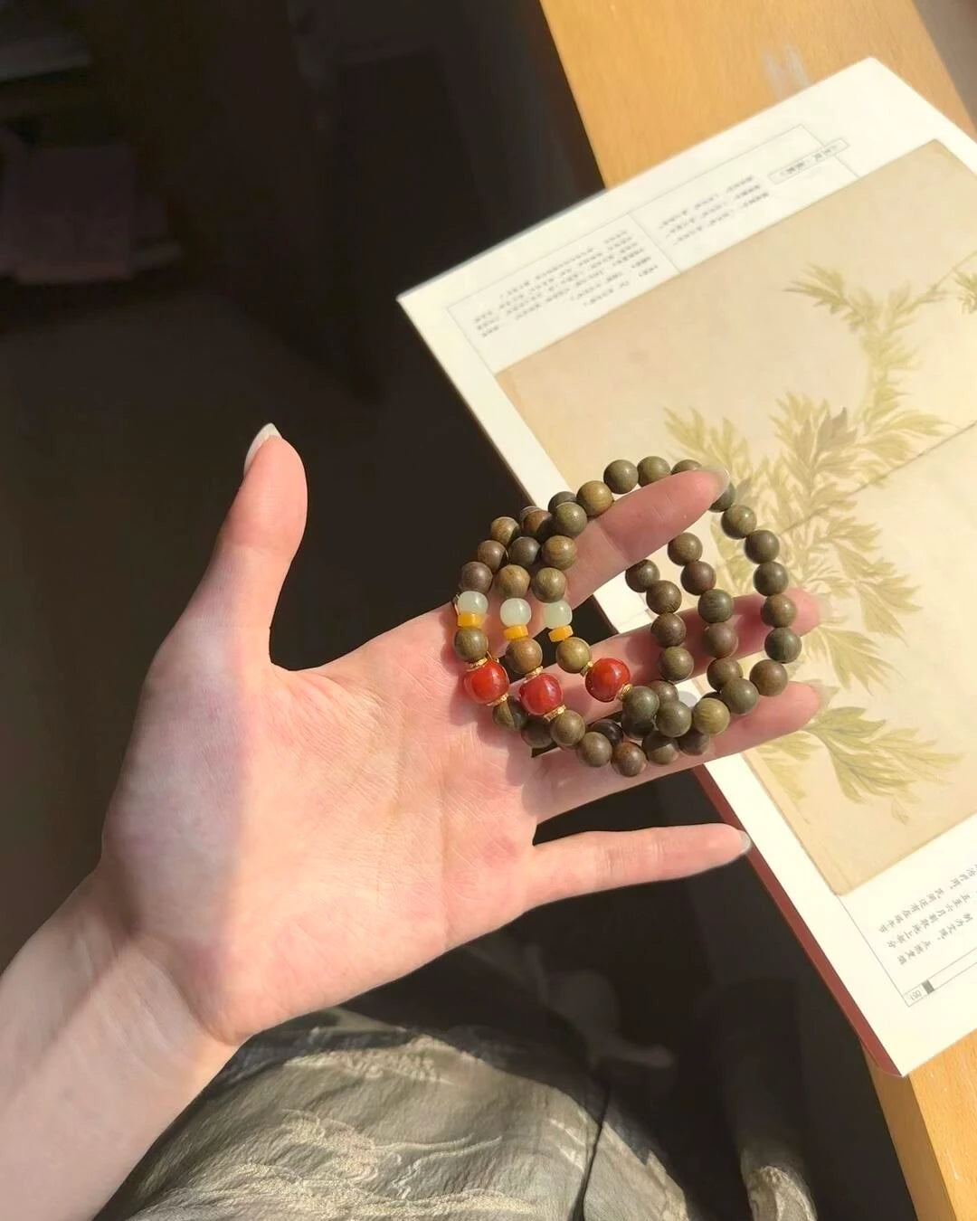 Three stacked Vital Harmony Bracelets in sunlight with sandalwood, red agate, amber, and jade beads.