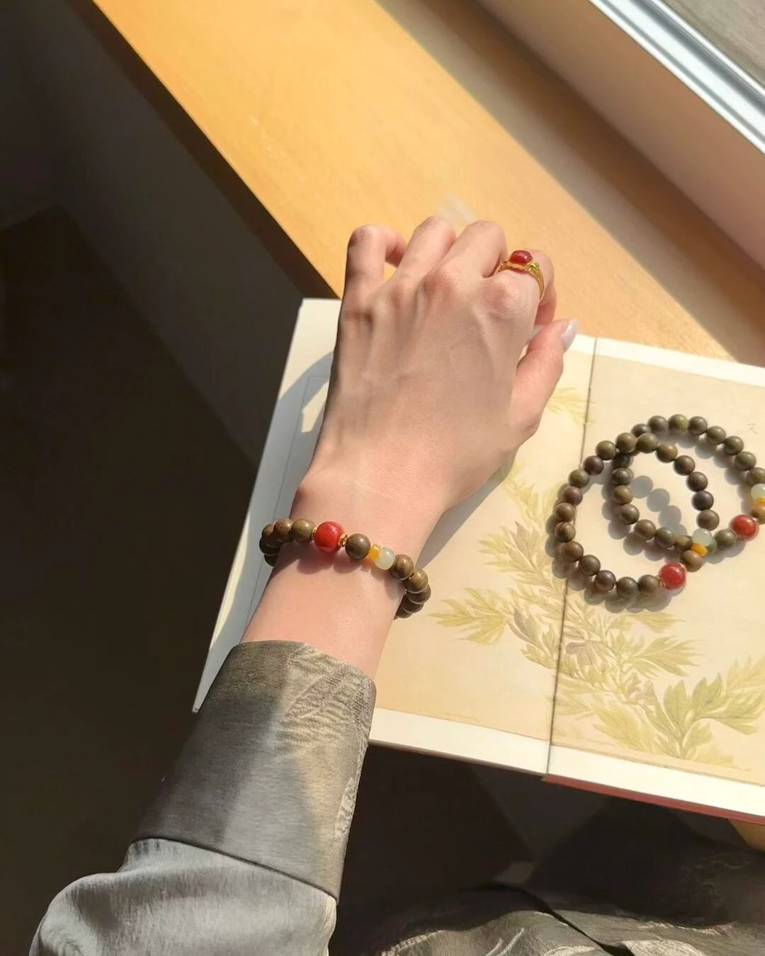Vital Harmony Bracelet worn at the windowsill with matching strands, featuring sandalwood and red agate beads.