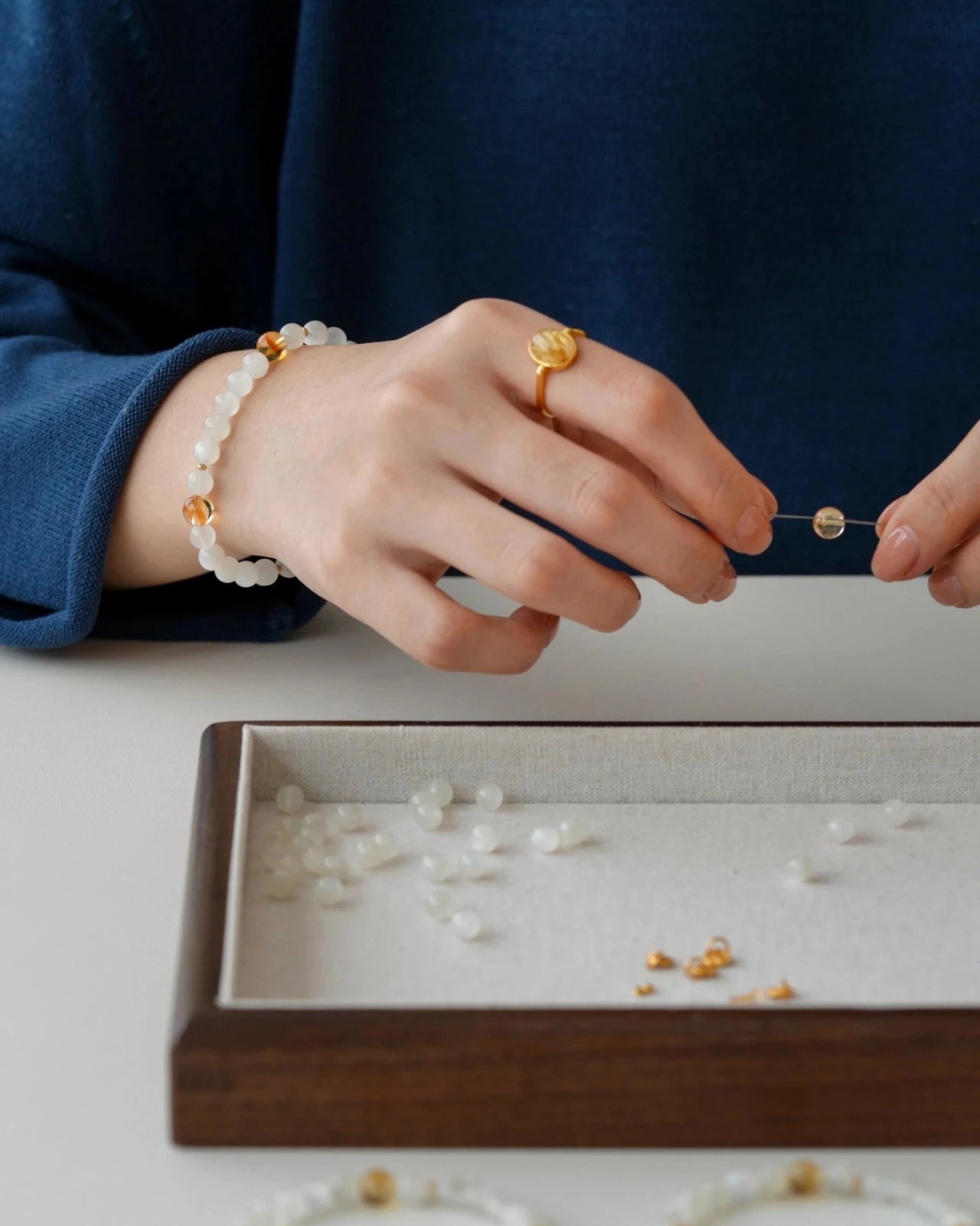 Handcrafted close-up—hands stringing white moonstone and citrine beads on elastic to make a beaded stretch bracelet.