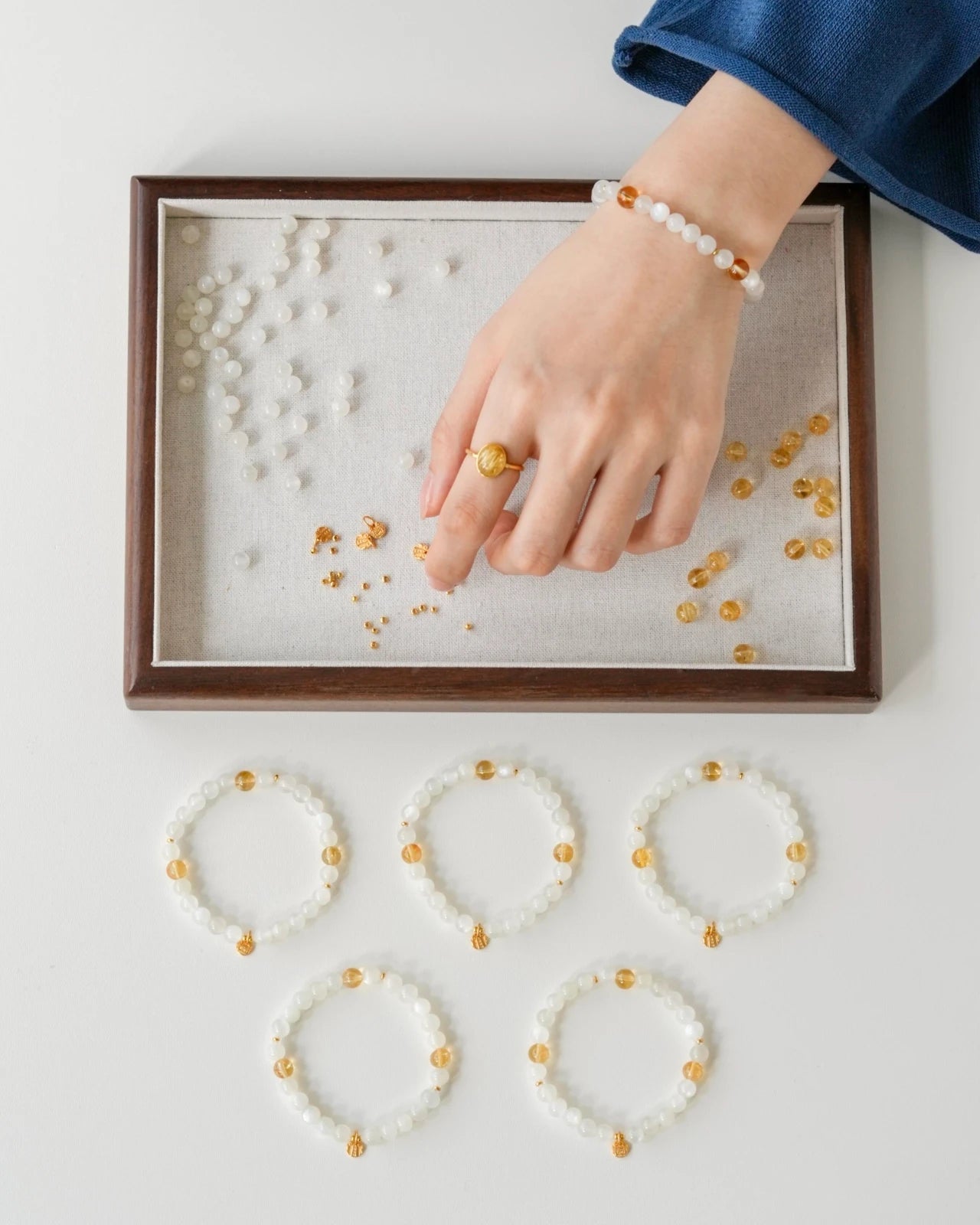 Studio wrist shot—white moonstone and citrine beaded stretch bracelet with a gold-plated S925 charm, hand above a bead tray.