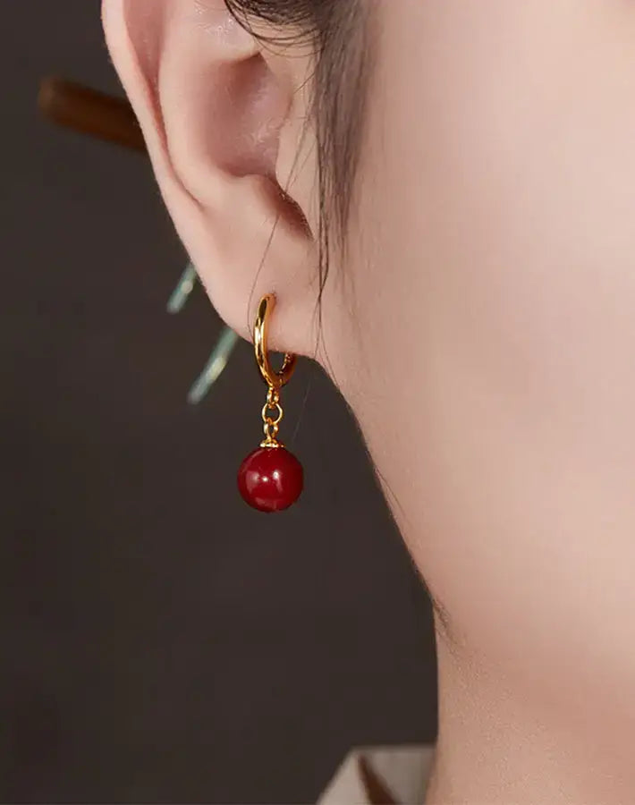 Close-up ear wearing a Red Aura earring featuring a cinnabar red bead and gold-plated S925 silver hoop.