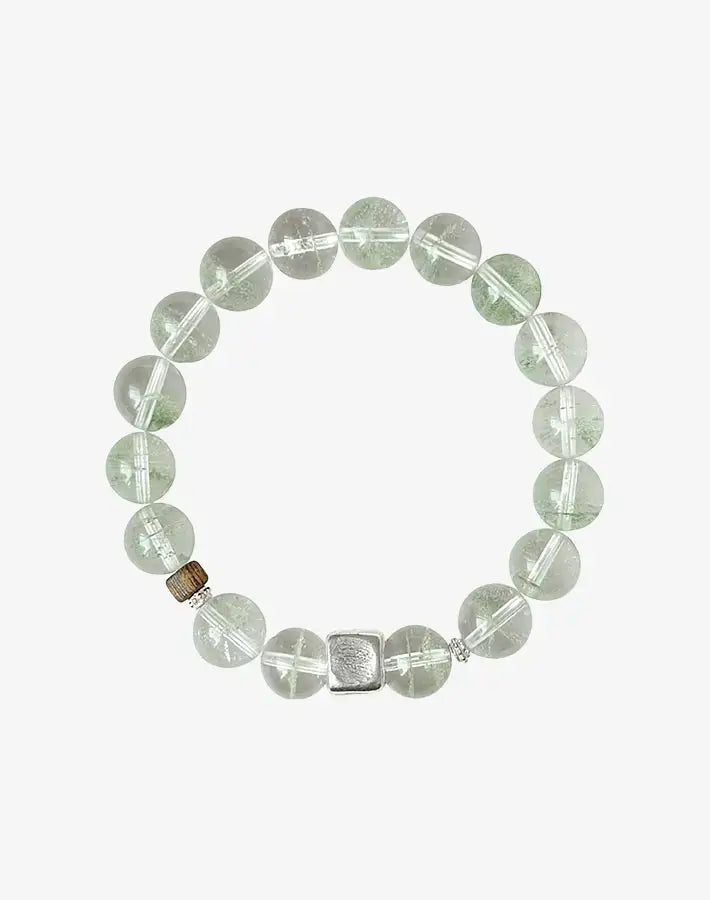 Isolated product shot of the Rooted Vision bracelet—green phantom quartz beads, natural agarwood accent, and central S925-silver cube spacer—on a gray background.