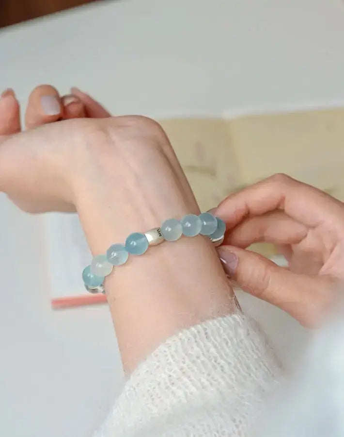 Wrist adjusting the Serenity Purity bracelet of aquamarine, white crystal and agarwood beads with a S925 silver cylinder accent.